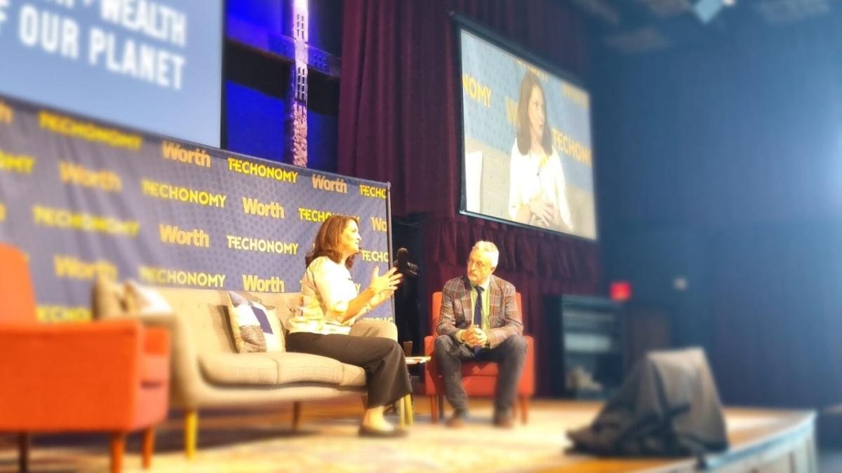 Heather Johnson and David Kirkpatrick seated on stage, a large screen behind them