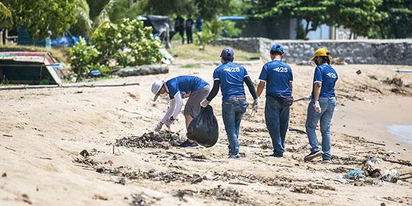 A group of people in matching shirts cleaning a beach.