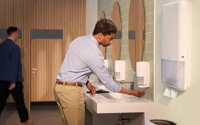 Office worker in a restroom using a soap dispenser.