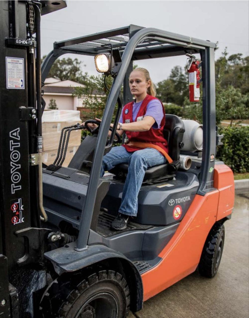 tractor supply employee in a red vest, driving a forklift