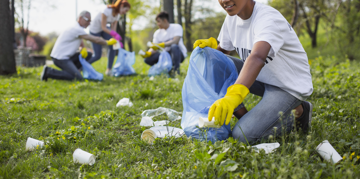 People kneeling down to pick up trash in a park like setting. They are wearing yellow protective gloves.