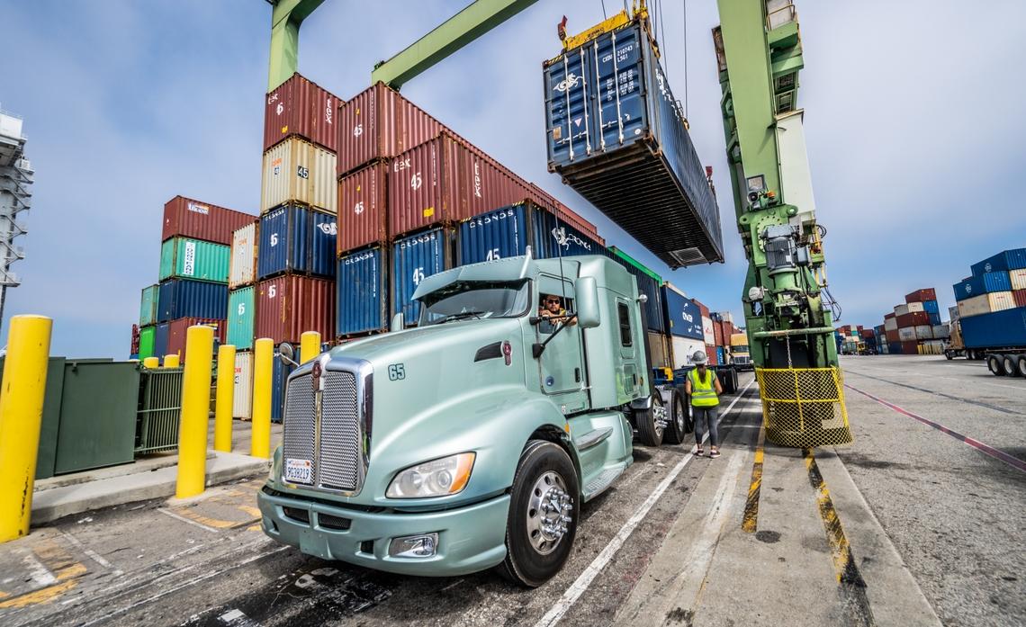 A large truck being loaded with a shipping container.