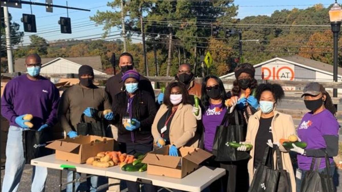 a group of people outside, a table in front of them with fruits and vegetables and boxes