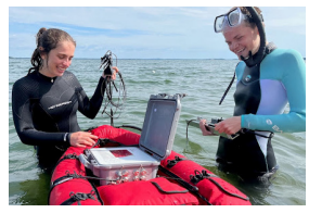 Two people standing in a body of water, devices on a small raft.