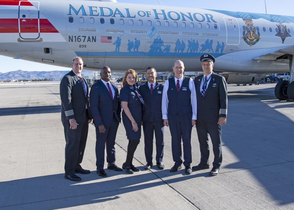 6 people in a line in flight uniforms. The Medal of Honor plane behind them.