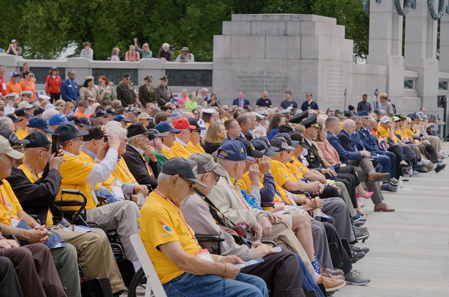 A seated crowd, many wearing the same yellow shirt designating them as a participant in the honor flight program