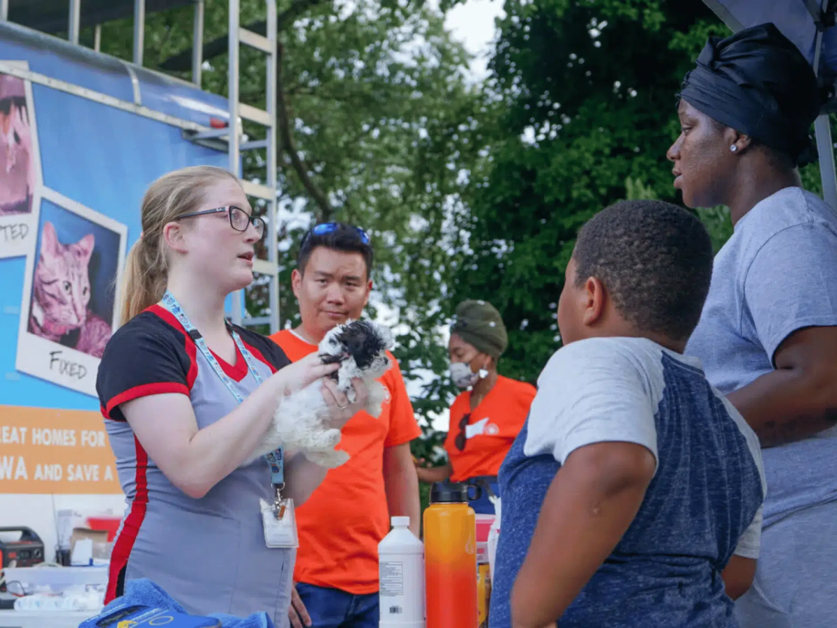 A worker holding a puppy and speaking with people