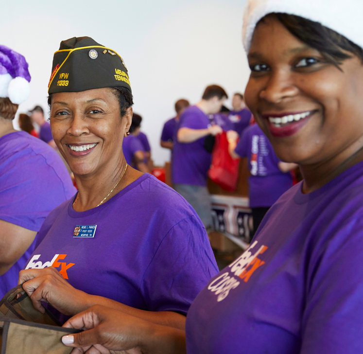 two people both wearing FedEx shirts, one has a military hat on