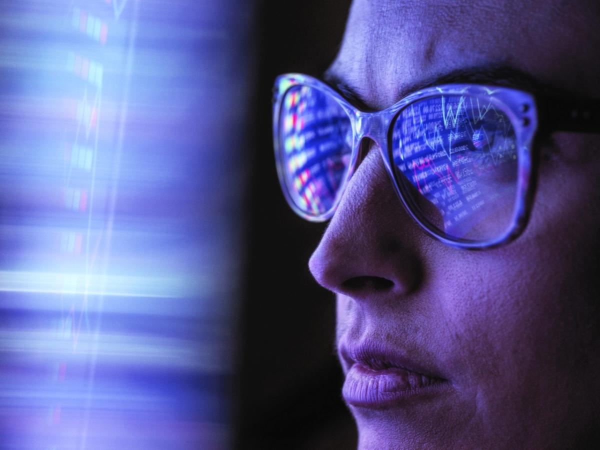 A person wearing glasses, computer data reflected in the lenses.