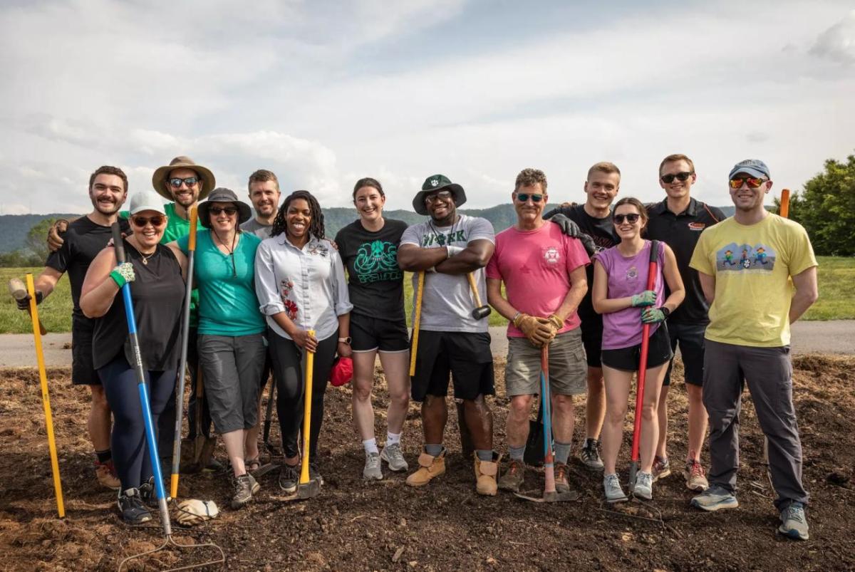 Group of volunteers stood together for a photo while holding gardening tools 