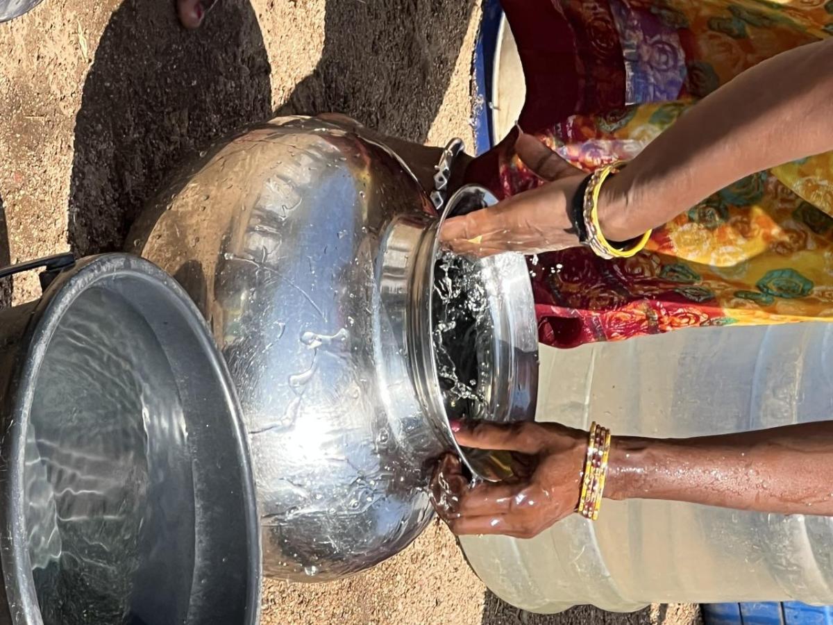 A person bent over washing a metal pot with water.