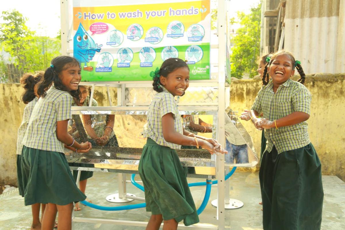 Smiling children washing their hands at a water station.