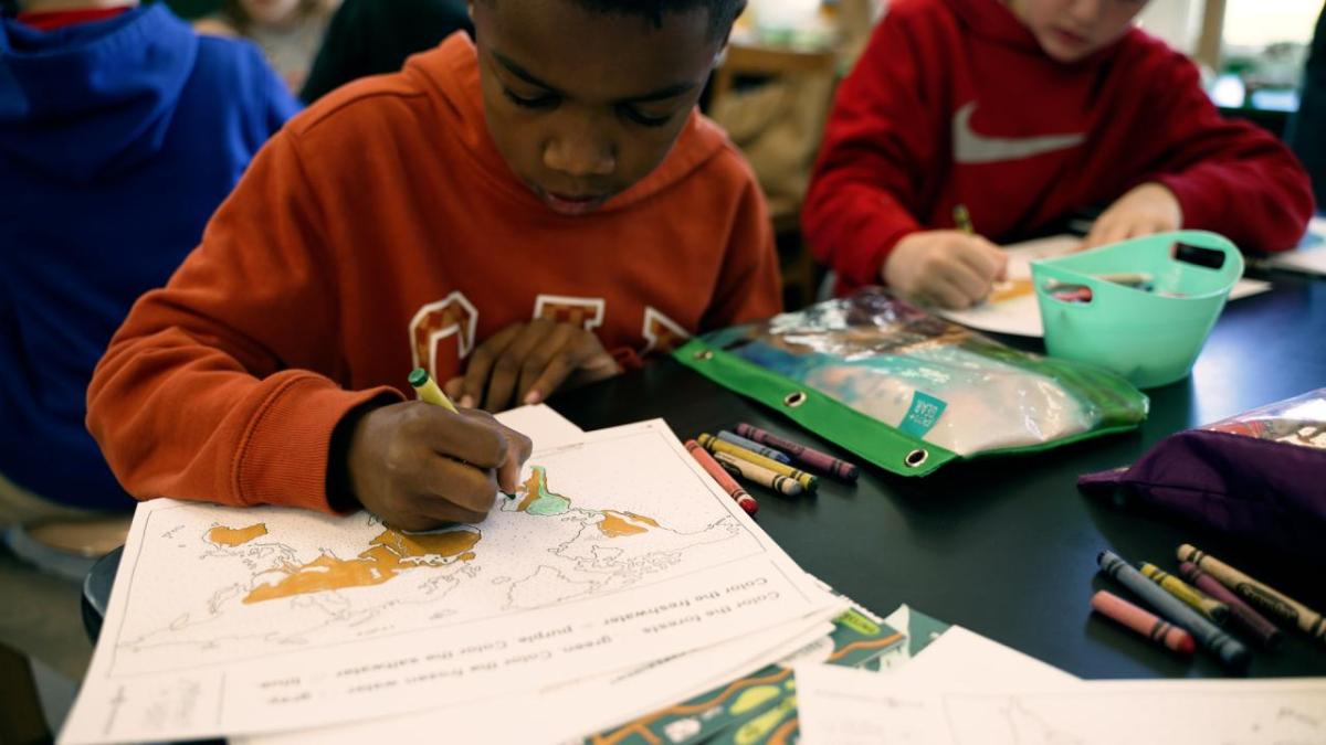 Children sat at a table colouring in sheets of paper