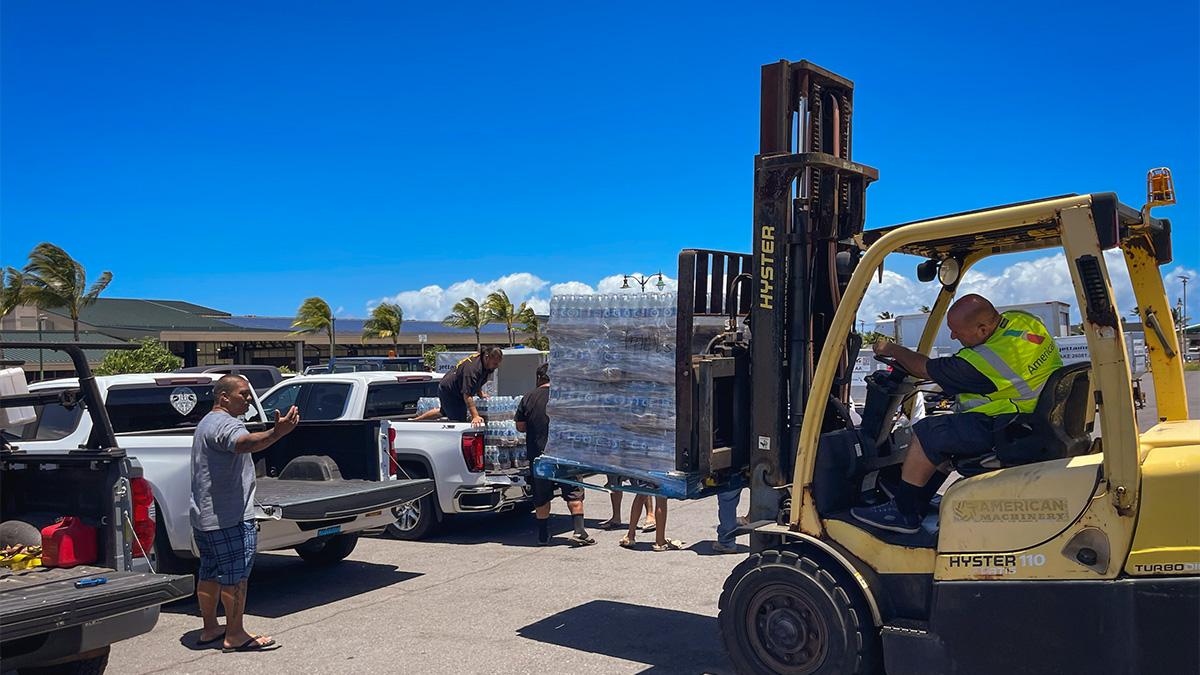 A forklife with pallets of water bottles being loaded into the back of a pickup truck.