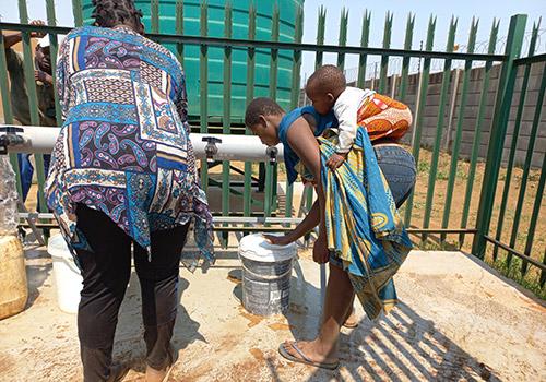 two people collect water, one carrying a child on their back