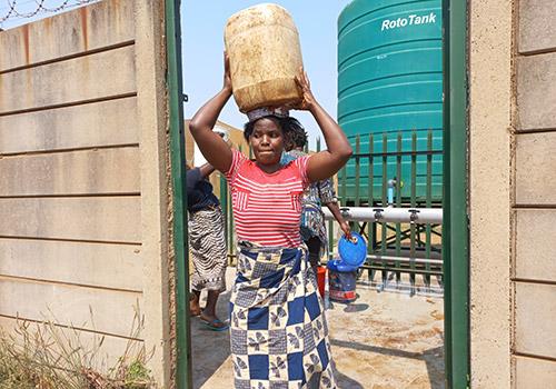 a person carrying a large jug on their head, a large tank behind them