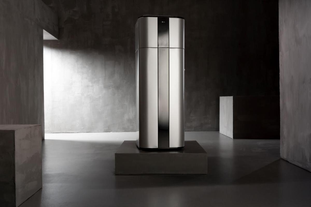 A sleek sliver and black heat pump machine on a grey square pedestal  in a stark smooth grey concrete room.
