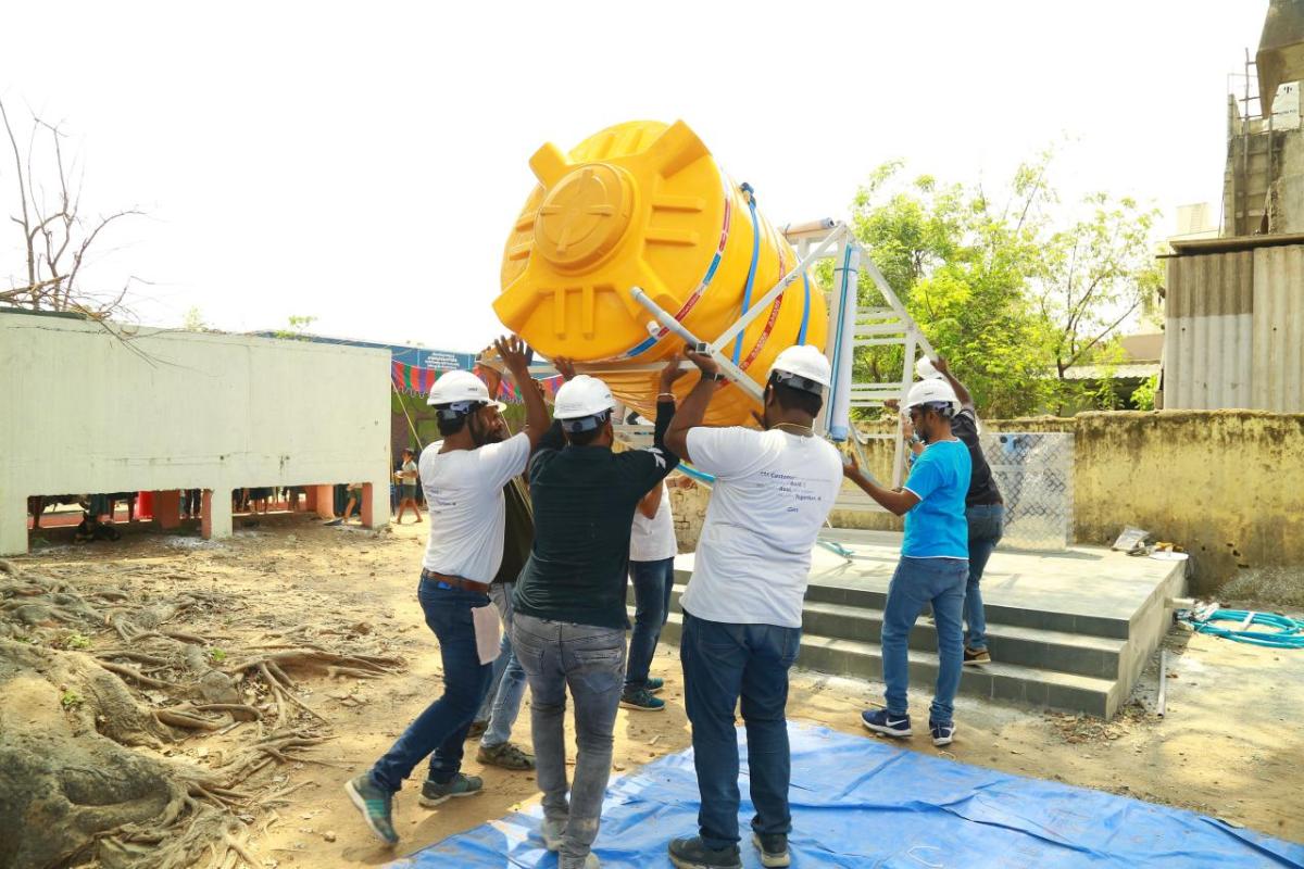 A group of adults in hard harts installing a tall water tank.