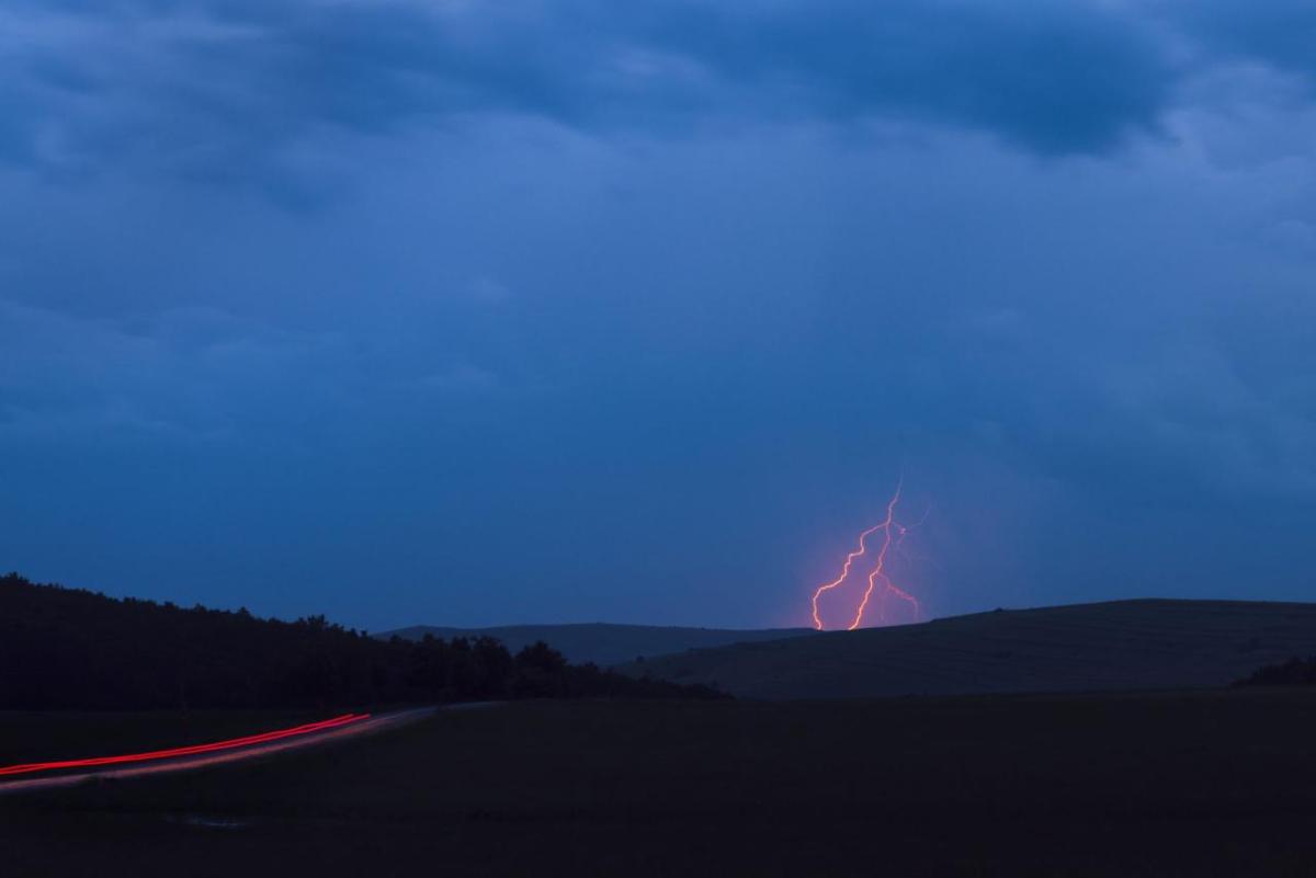 A cloudy sky with red lightning behind a distant hill