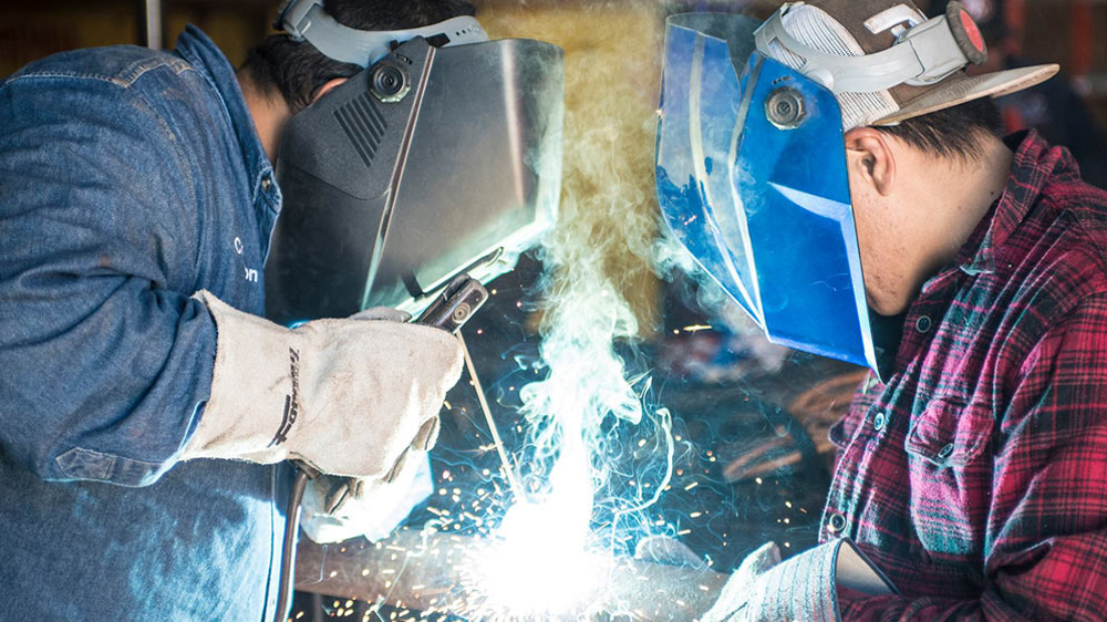 Two people in protective helmets and gloves, welding