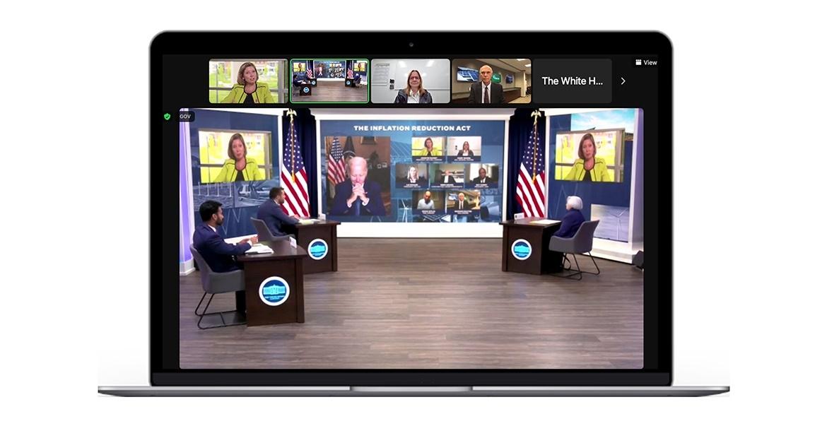 three people at desks in an open studio, multiple screens behind them with government officials appearing virtually