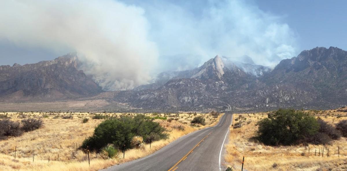 A mountain and desert landscape, billowing smoke from the hills