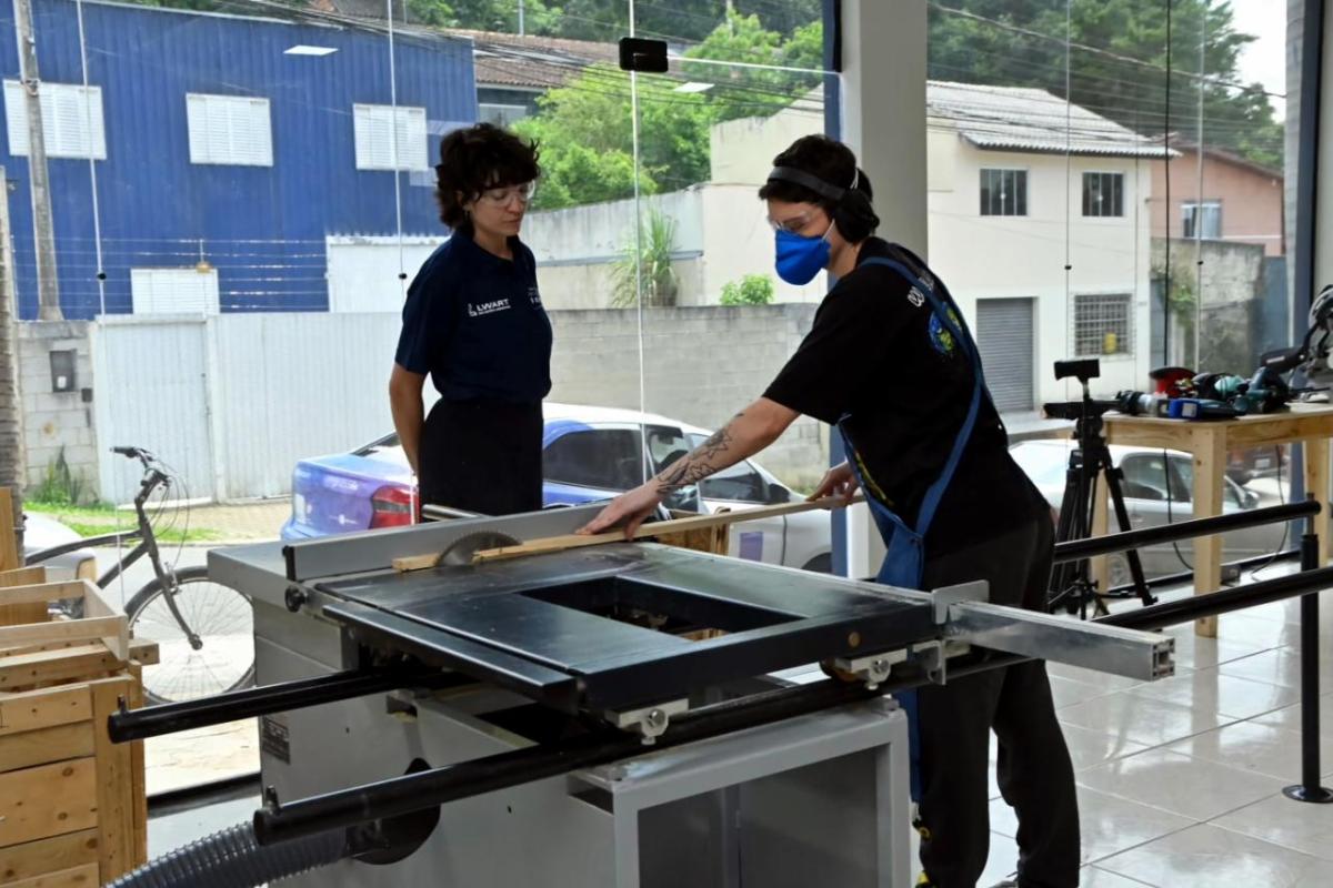 A student working at a wood saw as another looks on.