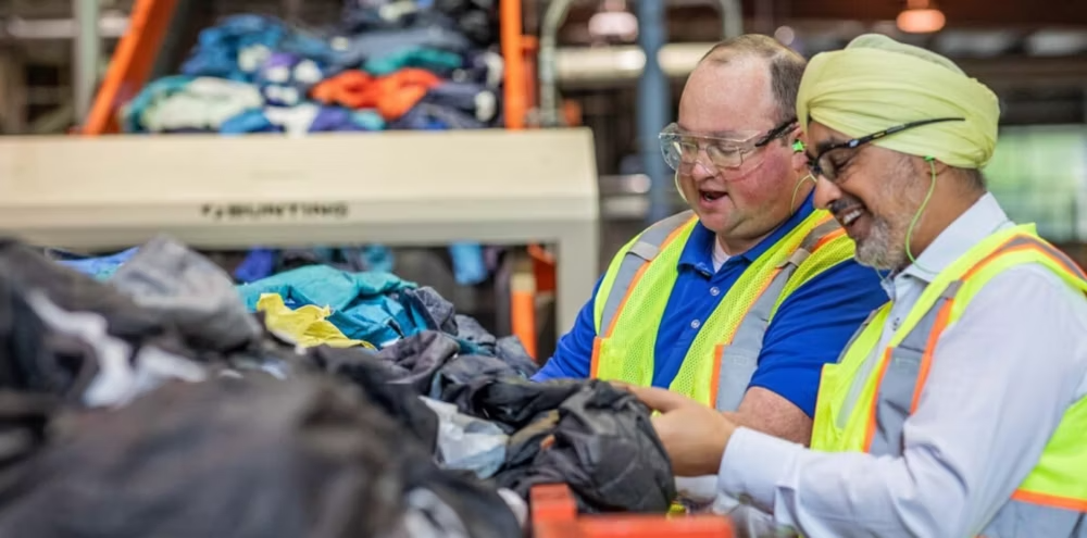 Two people in protective gear sort discarded textiles for recycling.