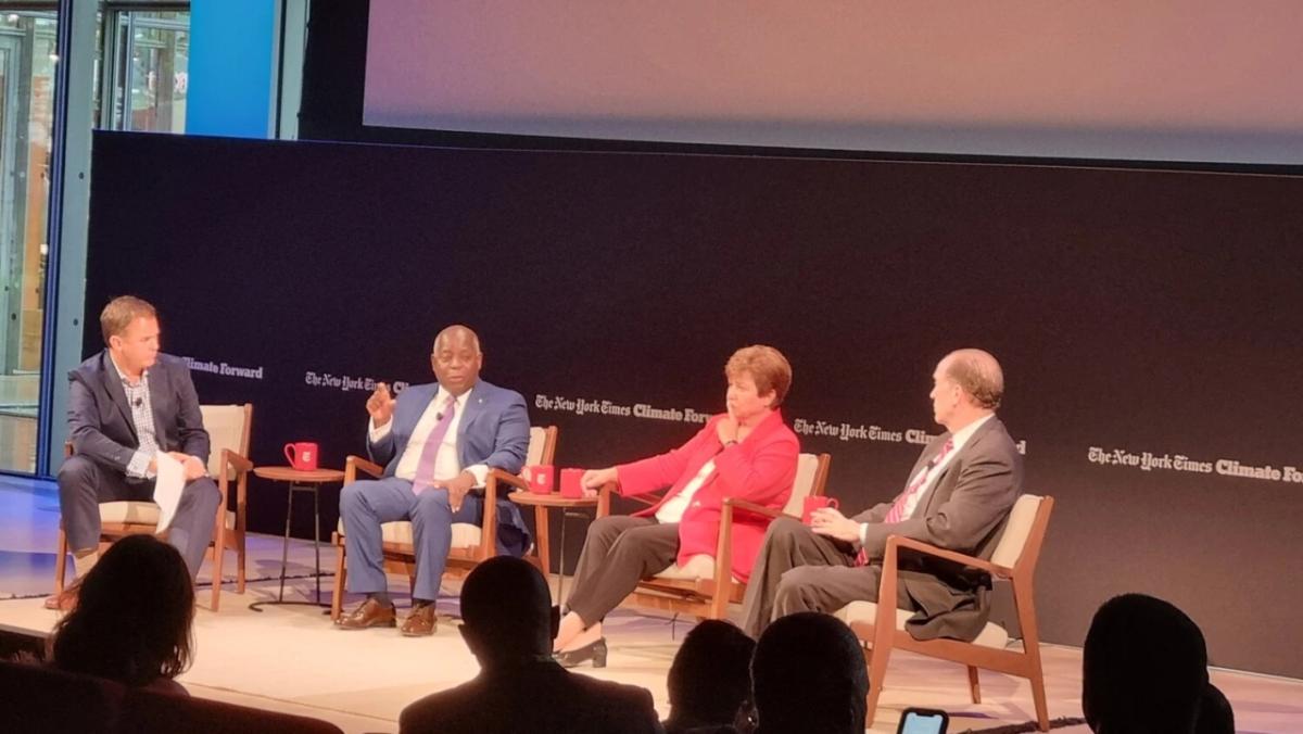 Four people sitting in a stage talking, an audience seated in front of them.