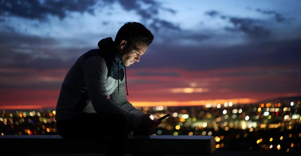 A person looking at a device in the dark. A city scape behind them.