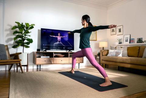 a person doing a yoga pose on a mat in a living room, watching an instructor on a tv screen