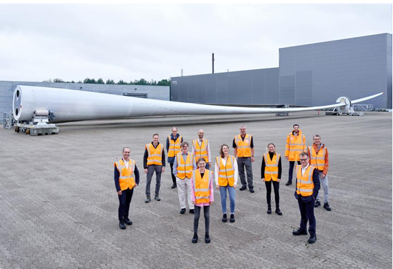The second ZEBRA blade seen at LM Wind Powers Lunderskov facility alongside consortium leaders. A group posed standing outside in front of a huge wind turbine blade.