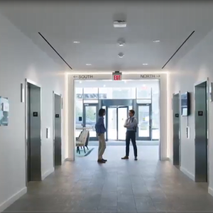 Two people at the end of an office hallway talking with each other.