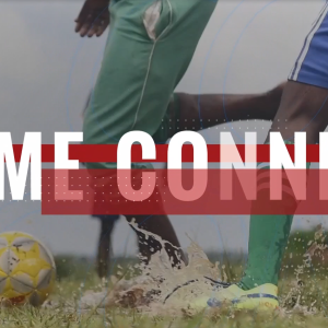 Two soccer players' legs and a soccer ball. Water splashes from the field.