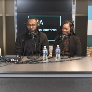 Four people with headsets and microphones, sitting at a desk.