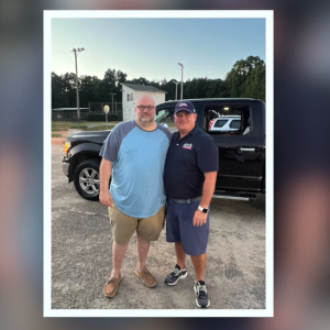 two men standing together in front of truck 