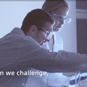 Two people in protective lab goggles, gloves and coats looking over beakers.