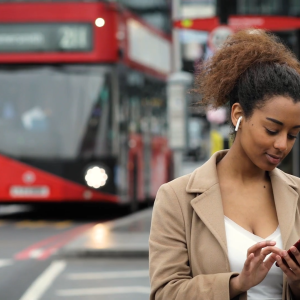 Person wearing wireless earbuds while using a phone with a red buss