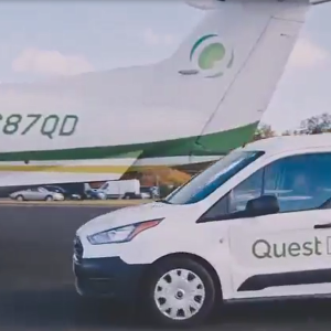 A white car with "Quest Diagnostics" on the side pulls up to a small plane with the same logo.