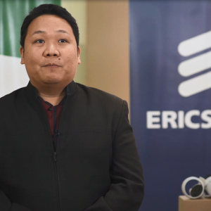 Dr. Bert Tuga sitting in front of an Ericsson sign, a VR headset to the right.