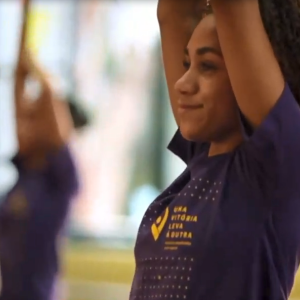 An athlete with both arms raised in a room with others doing the same in the background.