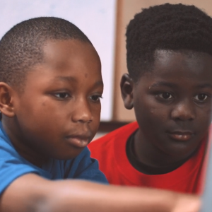 Two children looking at a laptop, one points to the screen.
