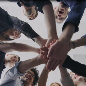 Looking up at a group of people each with a hand in the middle of a circle.