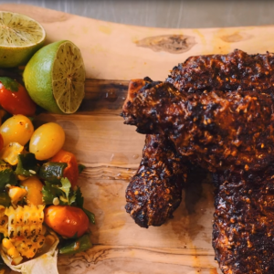 Plated dish of chicken with spices and vegetables and limes.