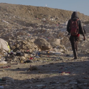 person walking away towards pile of garbage