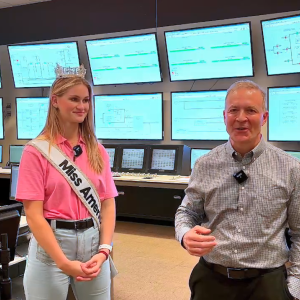 Grace wearing a crown and sash, and a representative from Southern Company in a room full of screens