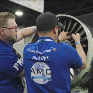 Two people working on an airplane engine, wearing matching shirts with American Airlines logo.