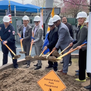 A group of people with hard hats and gold shovels in a ground breaking ceremony.