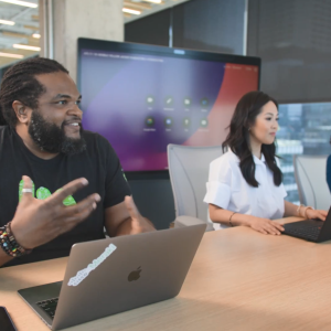 Three people at a long desk. A digital screen behind them.