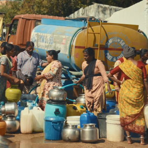A group of people collecting water from a truck with a water tank.